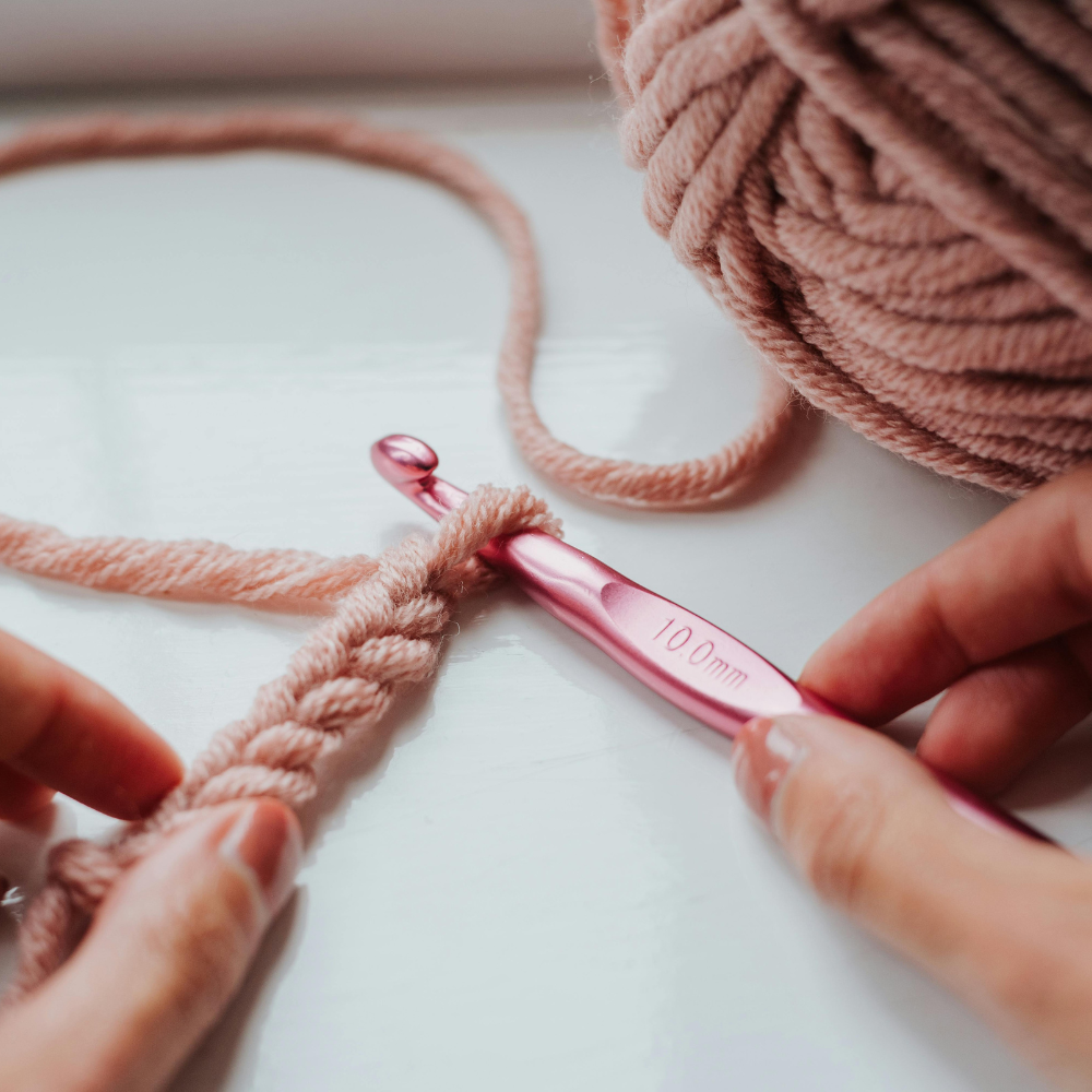 Manos trabajando una cadeneta a crochet con hilo rosa